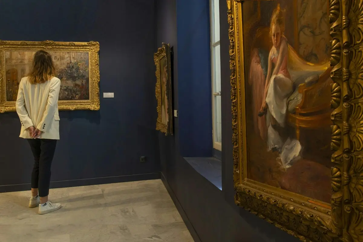 Une salle d'exposition aux murs bleus, où sont accrochés des tableaux encadrés, dont un portrait à droite et une autre œuvre d'art à gauche.
