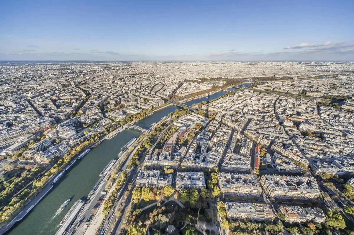 Vue aérienne d'une ville densément urbanisée, traversée par une rivière, avec des ponts enjambant le cours d'eau et des espaces verts disséminés un peu partout.