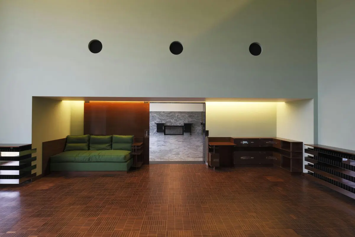 Un salon moderne avec un canapé vert, un sol en bois, des étagères murales et un bureau encastré contre un mur d'accent en marbre.