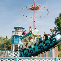 Personnes profitant d'un manège sur le thème du bateau, avec un phare et une grande balançoire en arrière-plan, sous un ciel dégagé. &copy; Walibi Rhone Alpes