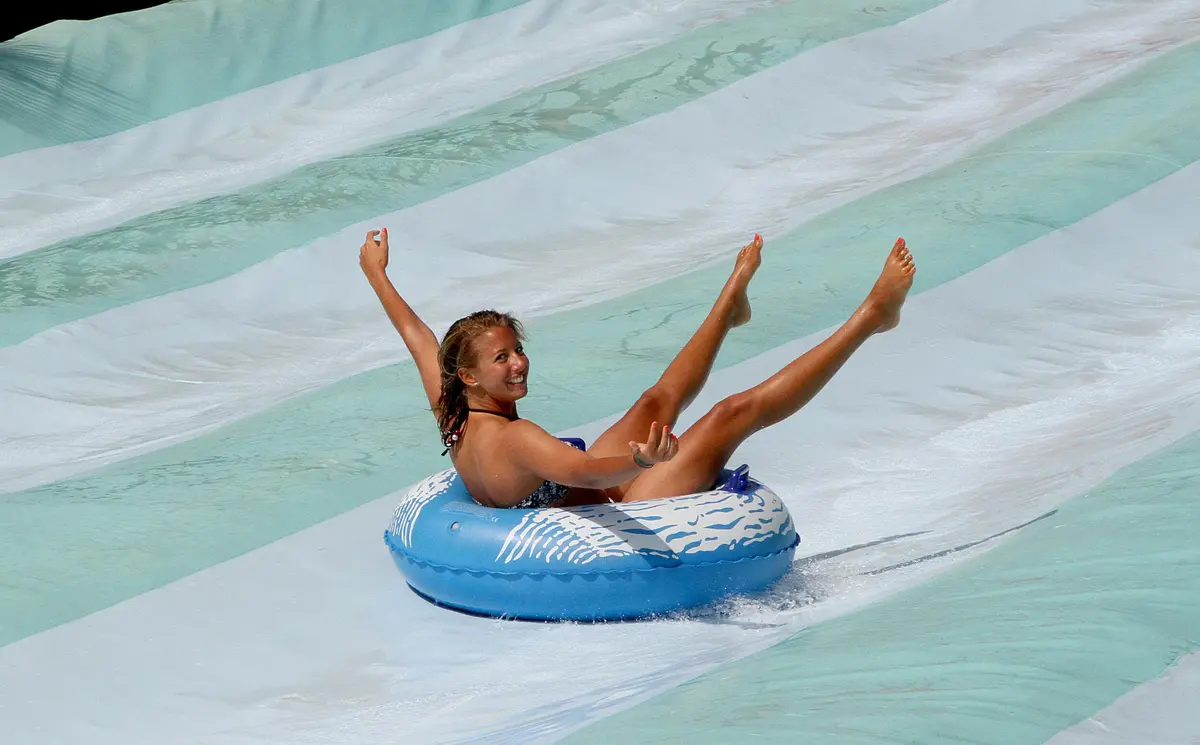 Une personne descend joyeusement un toboggan aquatique blanc et bleu clair sur un tube gonflable bleu.