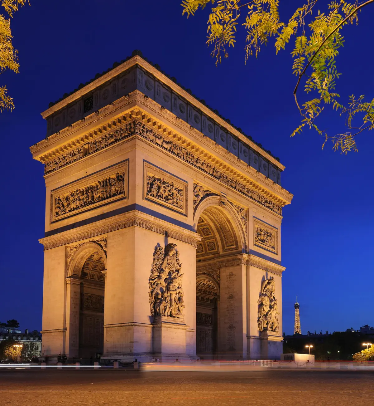 L'Arc de Triomphe illuminé dans un ciel crépusculaire, avec la Tour Eiffel visible à l'arrière-plan.