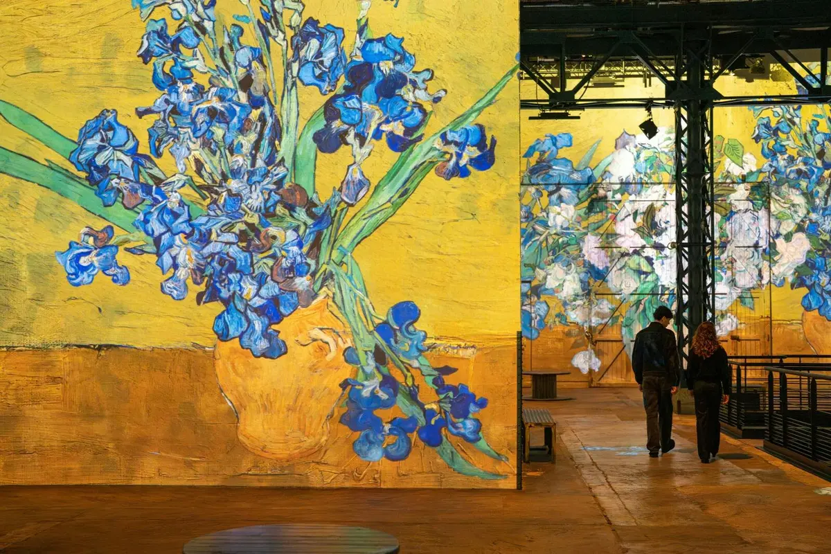 Une exposition d'art présentant des projections grand format du tableau de Van Gogh représentant des iris dans un vase jaune, avec une personne qui les contemple.