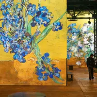 Une exposition d'art présentant des projections grand format du tableau de Van Gogh représentant des iris dans un vase jaune, avec une personne qui les contemple. &copy; Culturespaces___Cyrille_de_la_Motte_Rouge