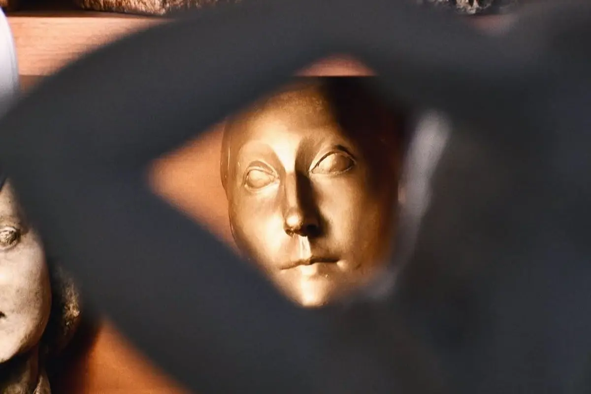 Un visage sculpté en or vu à travers un cadre sombre et flou avec un éclairage chaud.