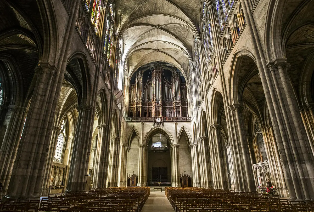 Intérieur d'une grande cathédrale avec des rangées de bancs en bois, des plafonds voûtés, des vitraux et un grand orgue.