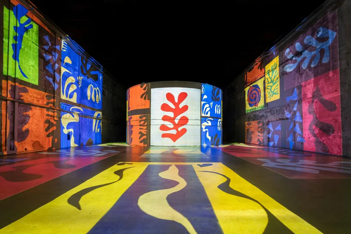 Une pièce dont les murs et le sol sont illuminés par des motifs abstraits colorés, avec au centre d'un écran une forme rouge ressemblant à une feuille.