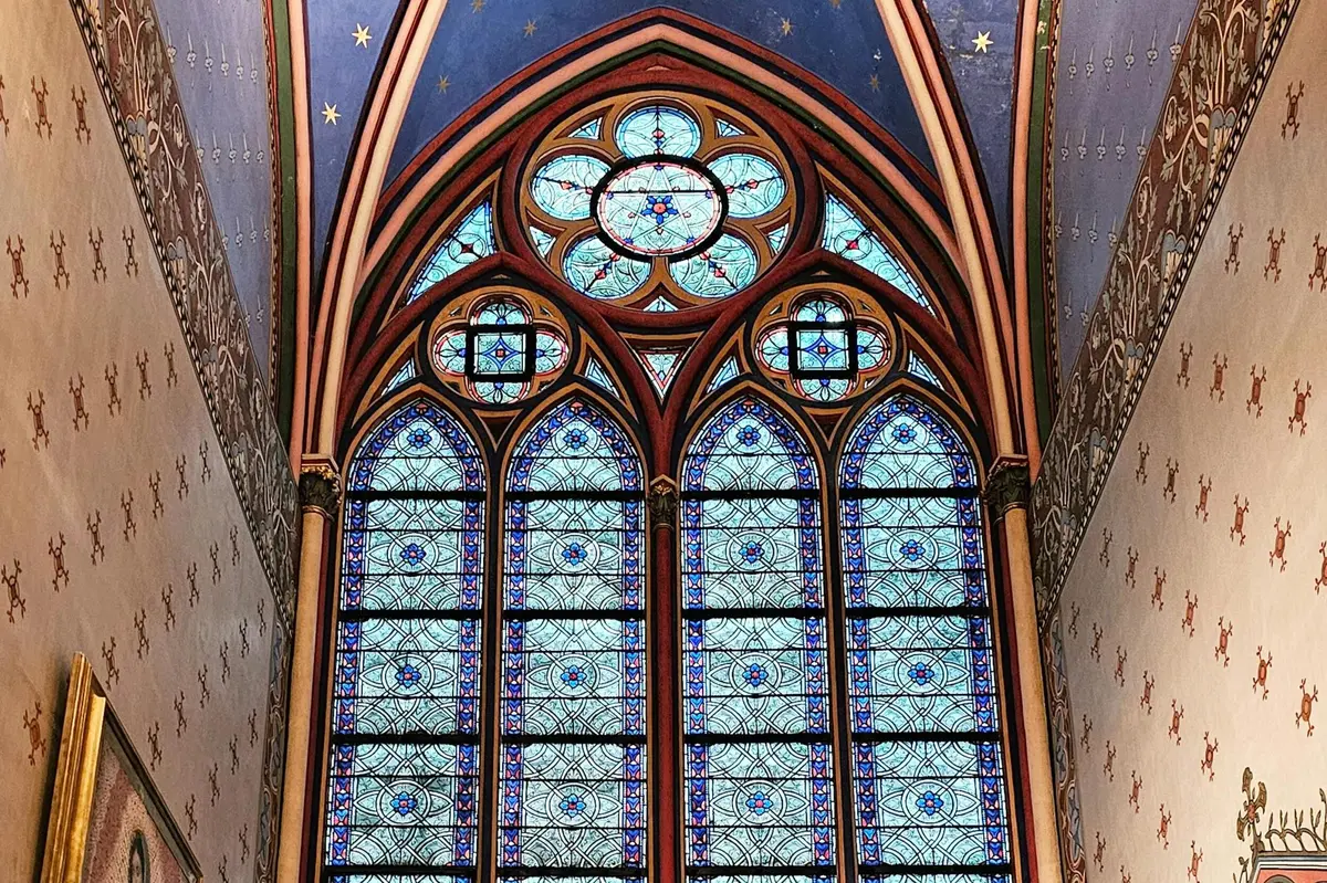 Vitraux aux motifs complexes bleus et rouges dans une cathédrale gothique à l'architecture arquée, avec un plafond bleu étoilé.
