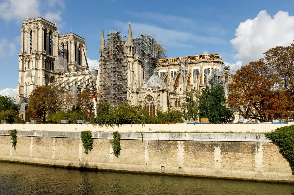 Bâtiment en cours de reconstruction avec échafaudage, vu de l'autre côté d'une rivière, sur fond de ciel bleu avec quelques nuages.