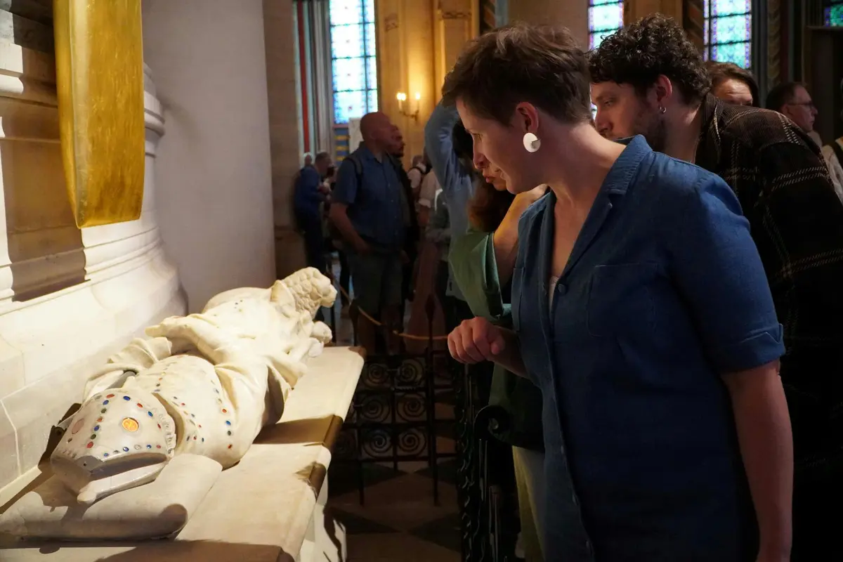 Personnes observant une sculpture en marbre blanc dans un musée avec des vitraux en arrière-plan.