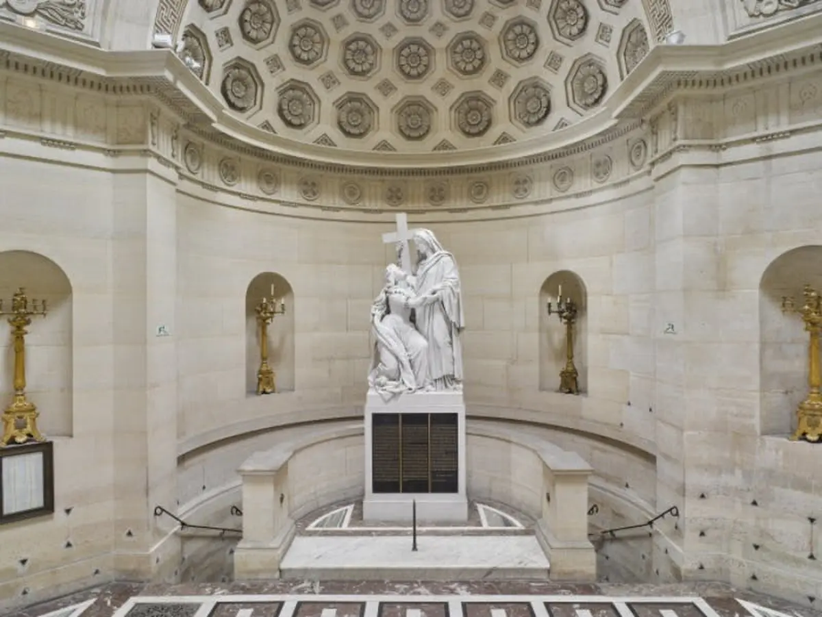 Intérieur orné d'une statue centrale en marbre représentant un personnage agenouillé et un personnage debout tenant une croix, flanqués de deux chandeliers en or.