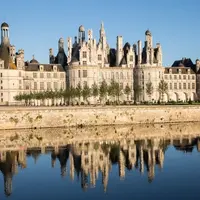 Château historique avec tours et tourelles ornées, se reflétant dans une rivière calme sous un ciel bleu clair. &copy; Sophie Lloyd