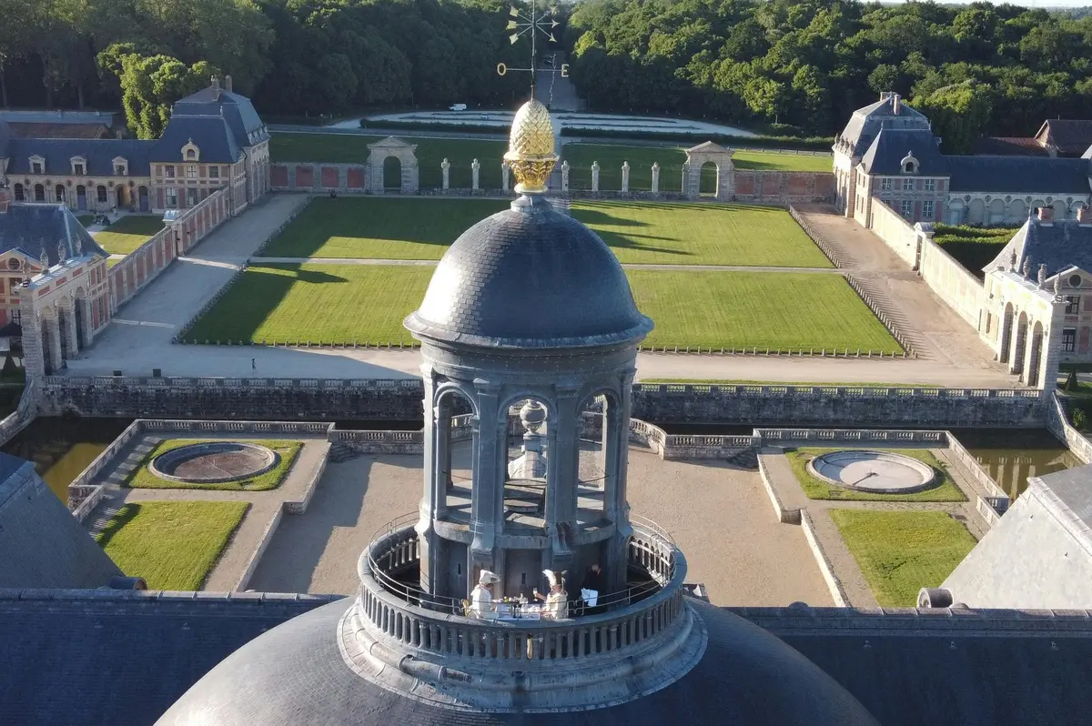 Vue aérienne d'un dôme surmonté d'un ornement en or, faisant partie d'un bâtiment historique entouré de jardins paysagers et d'arbres.