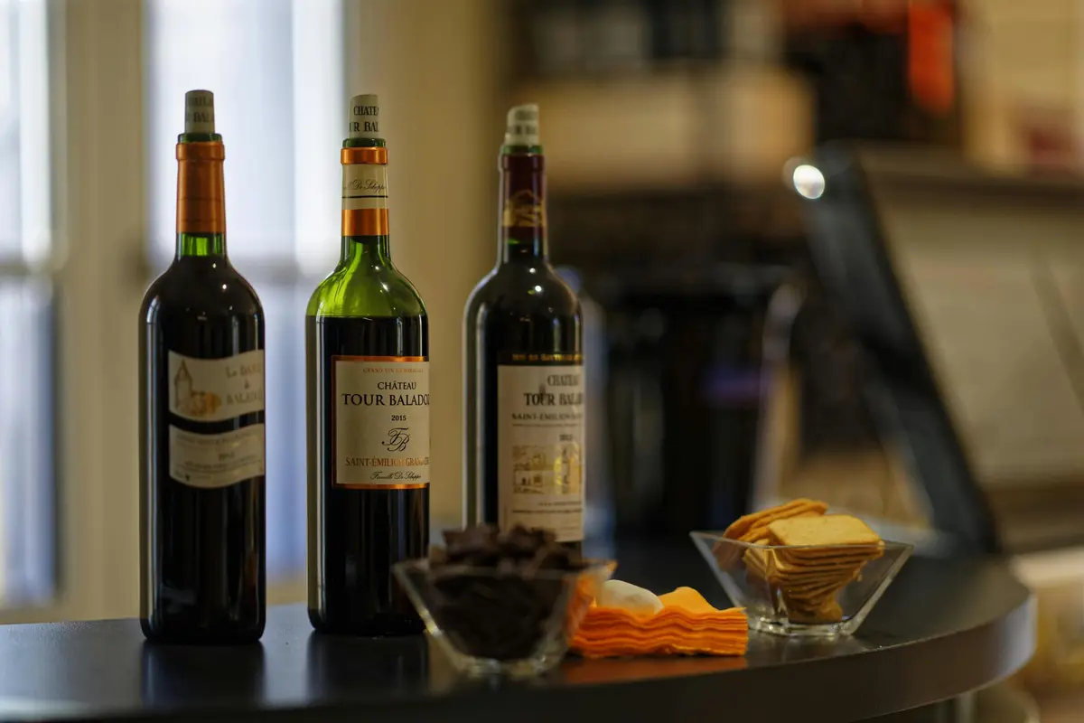 Trois bouteilles de vin, deux bols d'amuse-gueule et des serviettes pliées sur une surface noire dans un endroit peu éclairé.