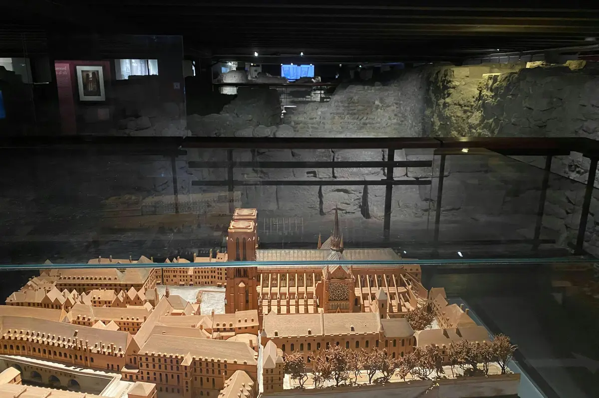 Une maquette en bois détaillée d'une ville médiévale avec une grande cathédrale est exposée dans une vitrine dans une pièce faiblement éclairée.