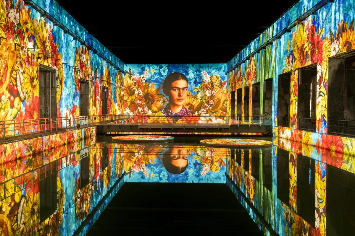 Un grand espace intérieur avec des projections colorées de fleurs et le portrait d'une femme se reflétant sur une surface d'eau lisse.