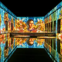 Un grand espace intérieur avec des projections colorées de fleurs et le portrait d'une femme se reflétant sur une surface d'eau lisse. &copy; @Culturespaces / Geoffroy Groult