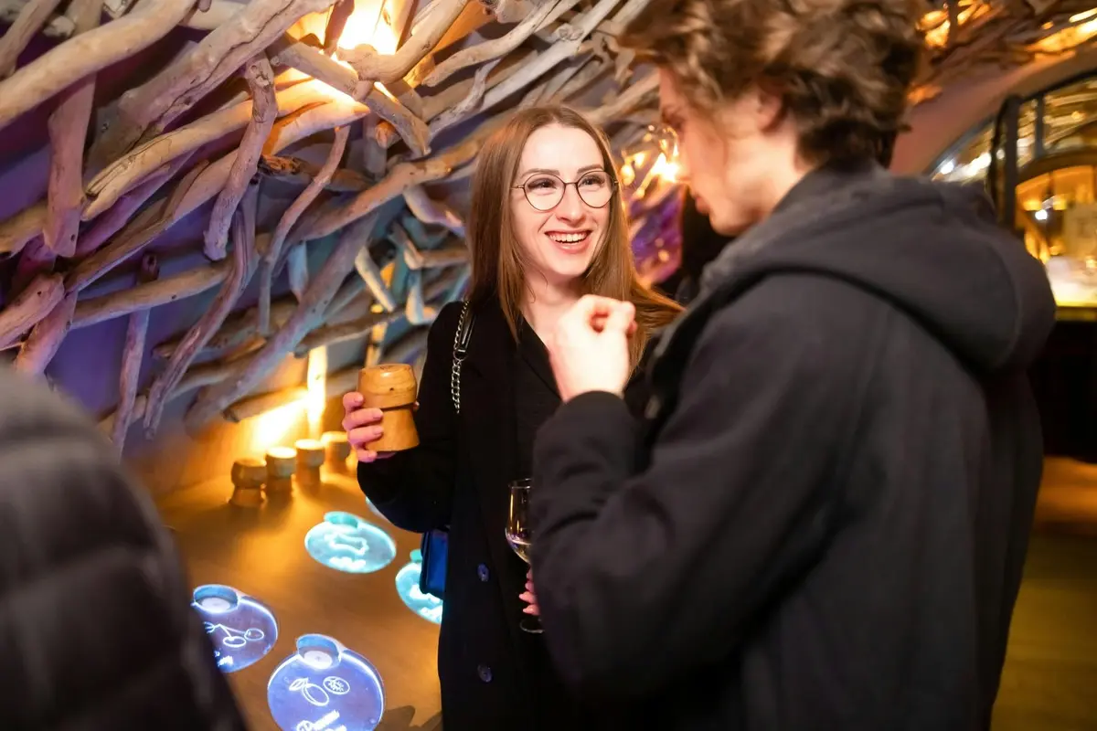 Deux personnes en conversation dans un lieu décoré avec des écrans bleus lumineux, l'une tenant un verre et souriant.