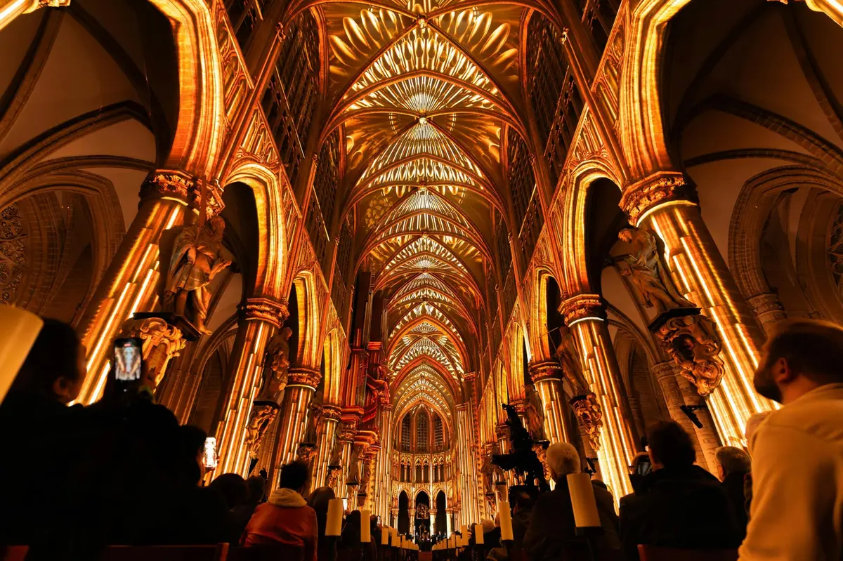 Intérieur d'une grande cathédrale baigné d'une lumière chaude et décorative, avec des personnes assises sur les bancs sous les voûtes.