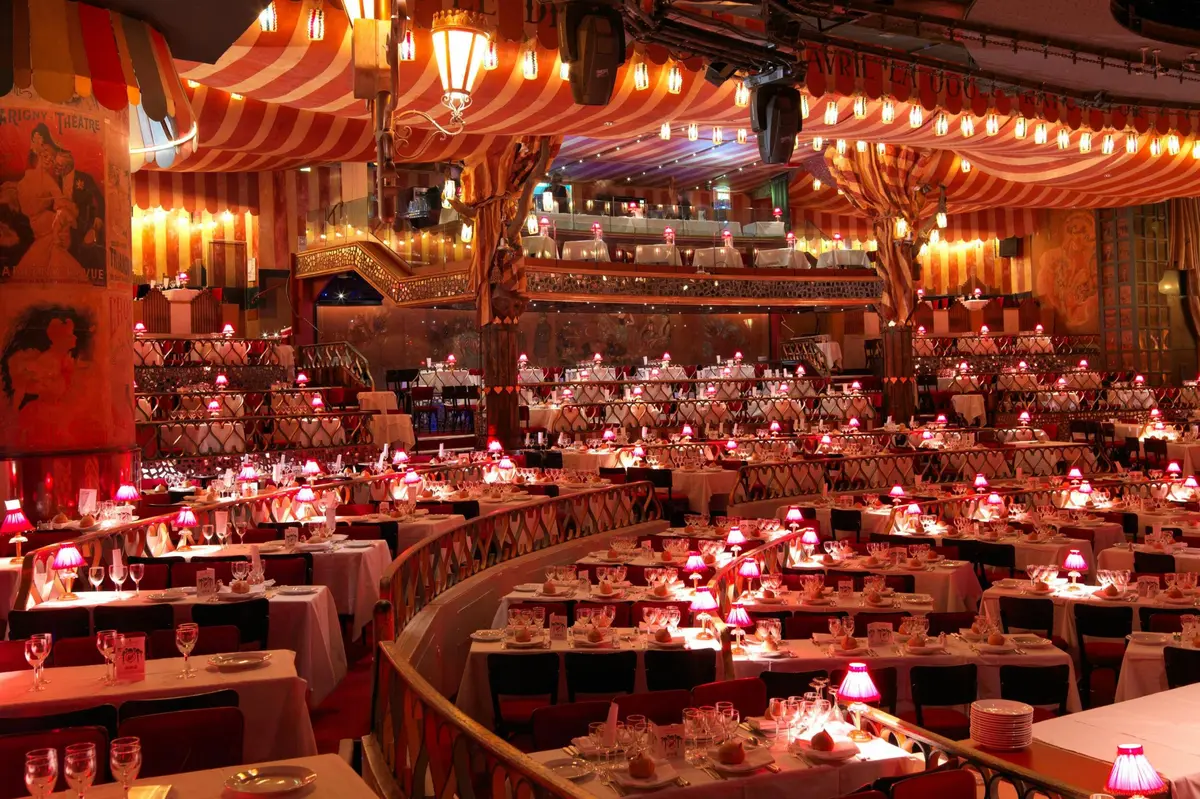 Un lieu somptueusement décoré, avec de nombreuses tables, un éclairage rouge et un décor raffiné sous un plafond rayé.