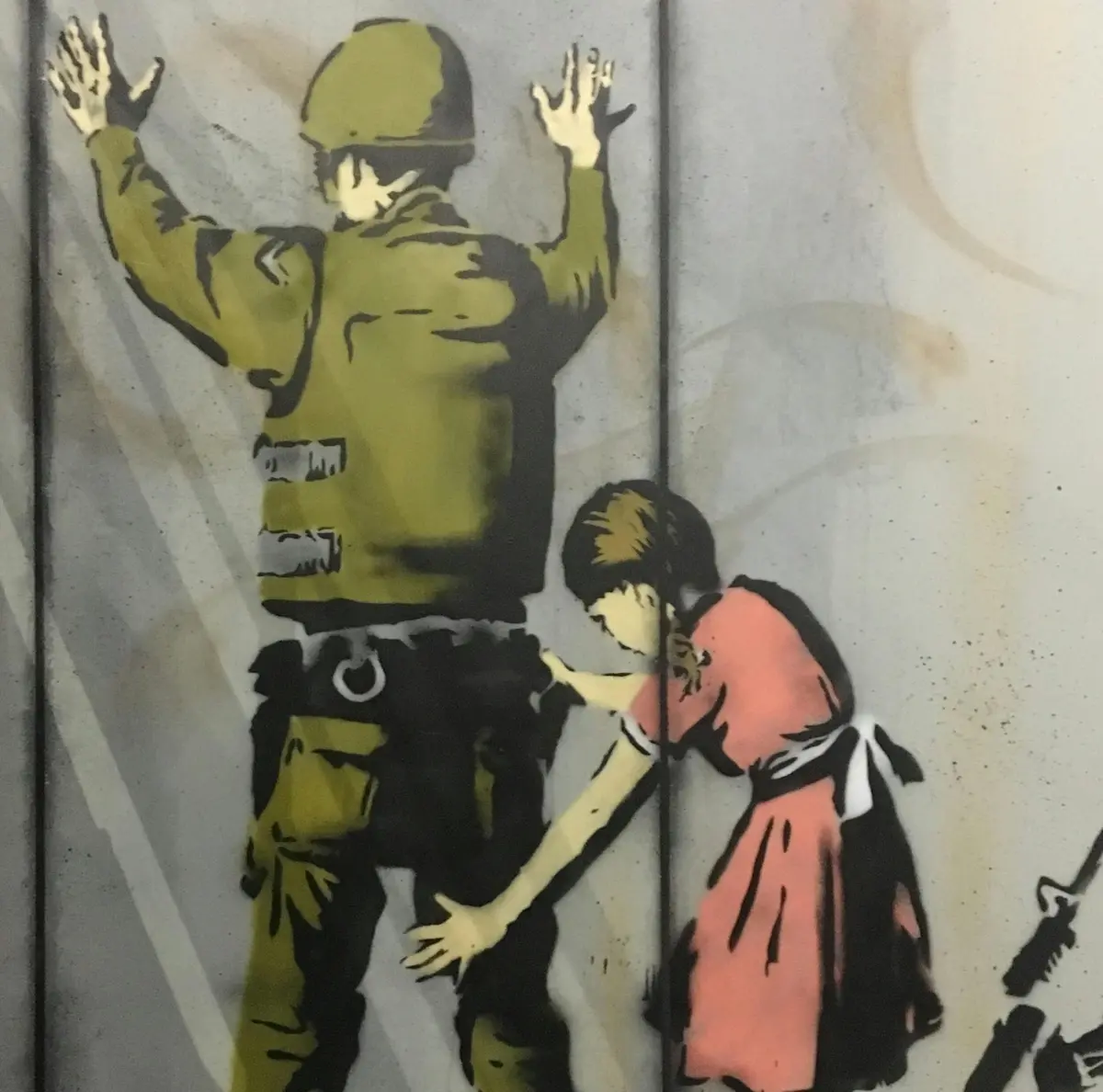 Graffiti représentant un soldat fouillé par une jeune fille. Le soldat a les mains en l'air et la jeune fille porte une robe rose.