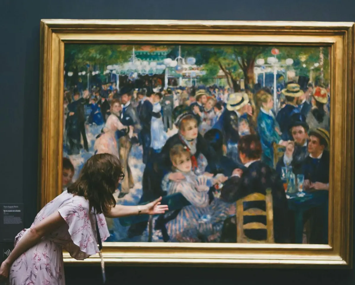 Une femme se penche vers un grand tableau encadré représentant une réunion sociale animée en plein air avec de nombreuses personnes en vêtements d'époque.