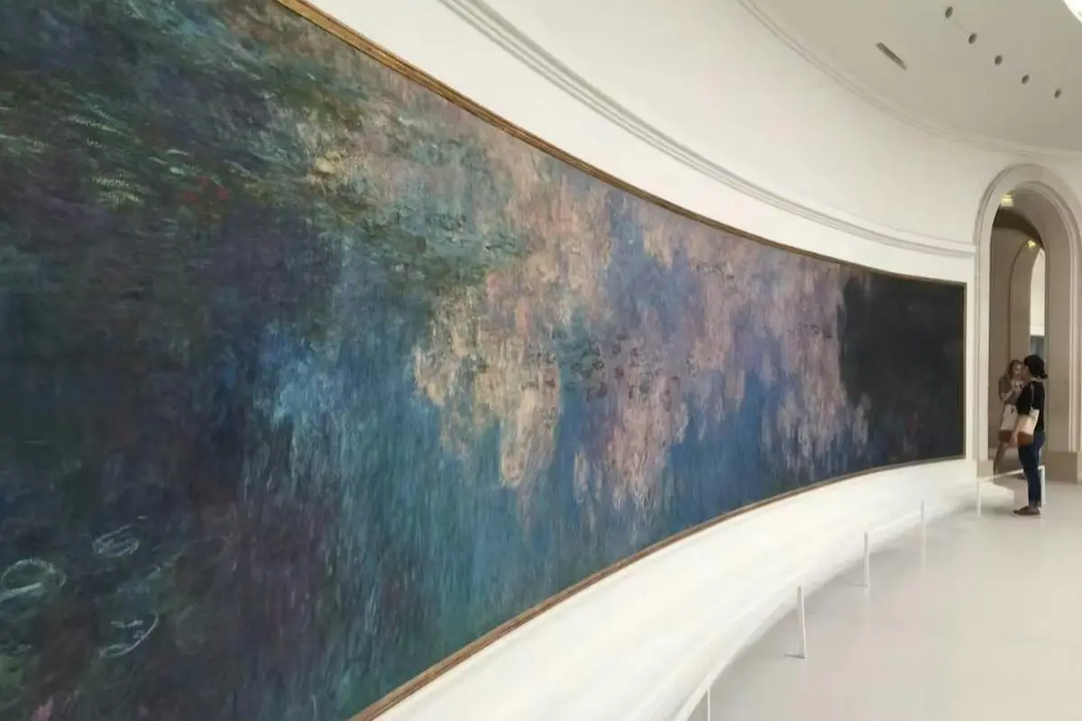 Un grand tableau accroché au mur représentant une scène abstraite de nénuphars dans la salle d'un musée, avec des bancs incurvés en contrebas.