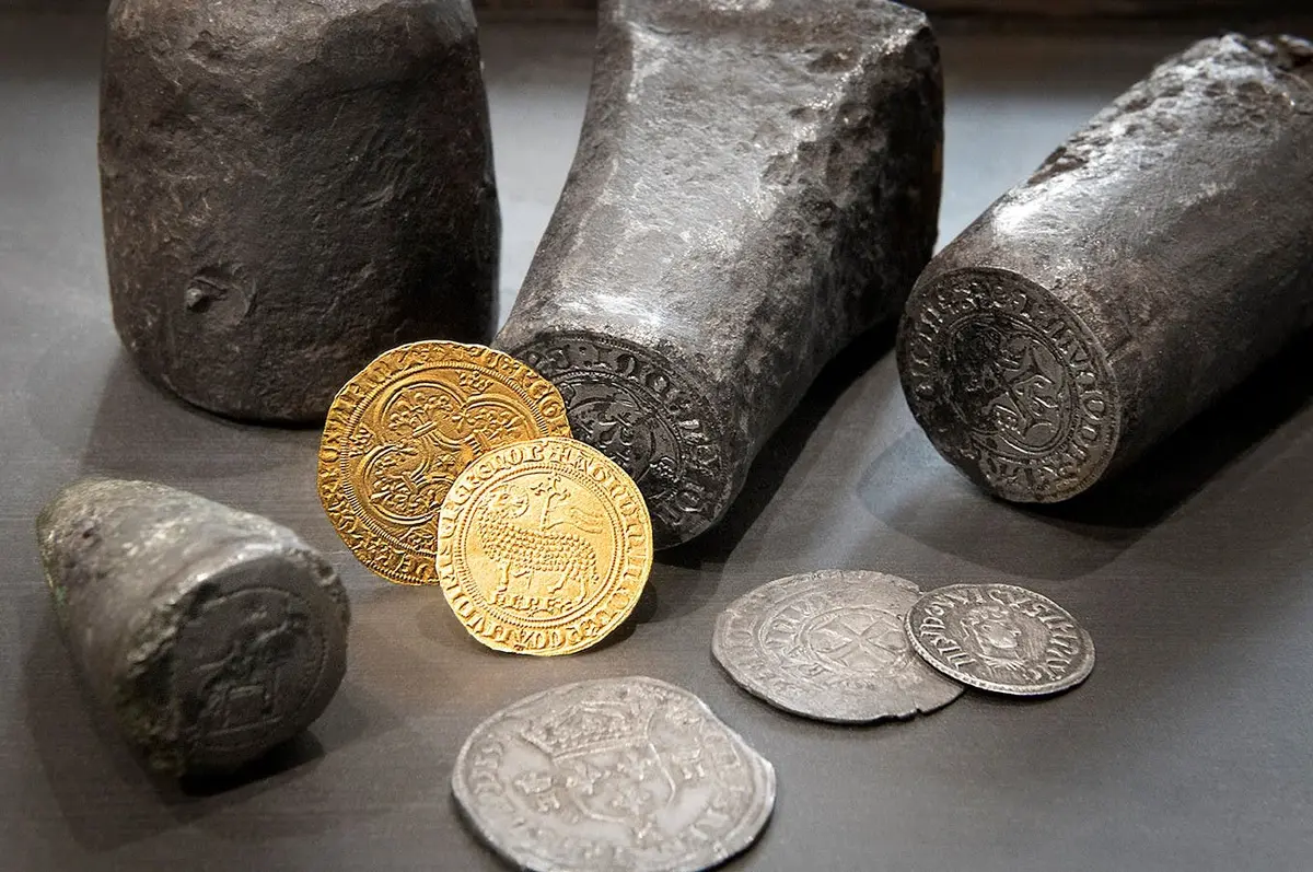 Pièces d'or et d'argent anciennes placées devant des cachets médiévaux sur une surface sombre.