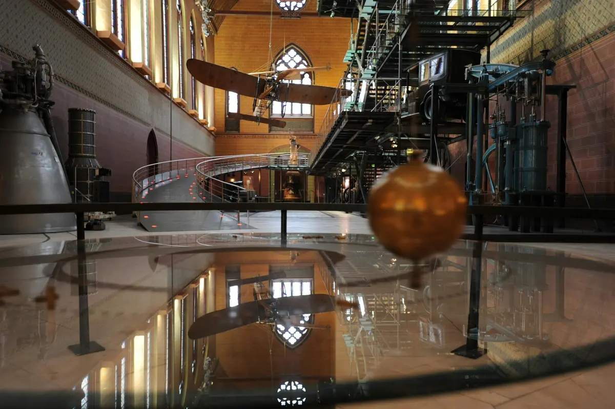 Un pendule est vu à l'intérieur d'un bâtiment de style industriel avec des murs en briques, des fenêtres cintrées et des escaliers en fer.