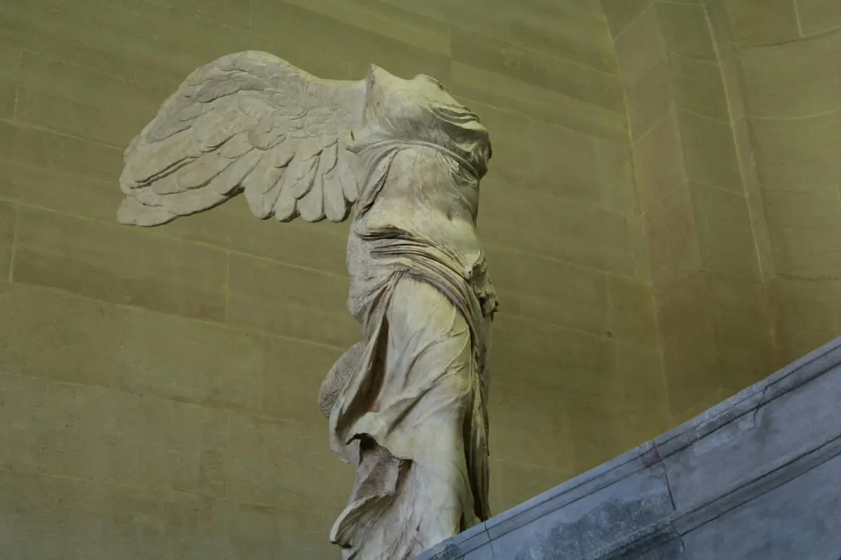 Statue en marbre d'un personnage ailé, sans tête, drapé dans des vêtements fluides, exposée dans un musée.