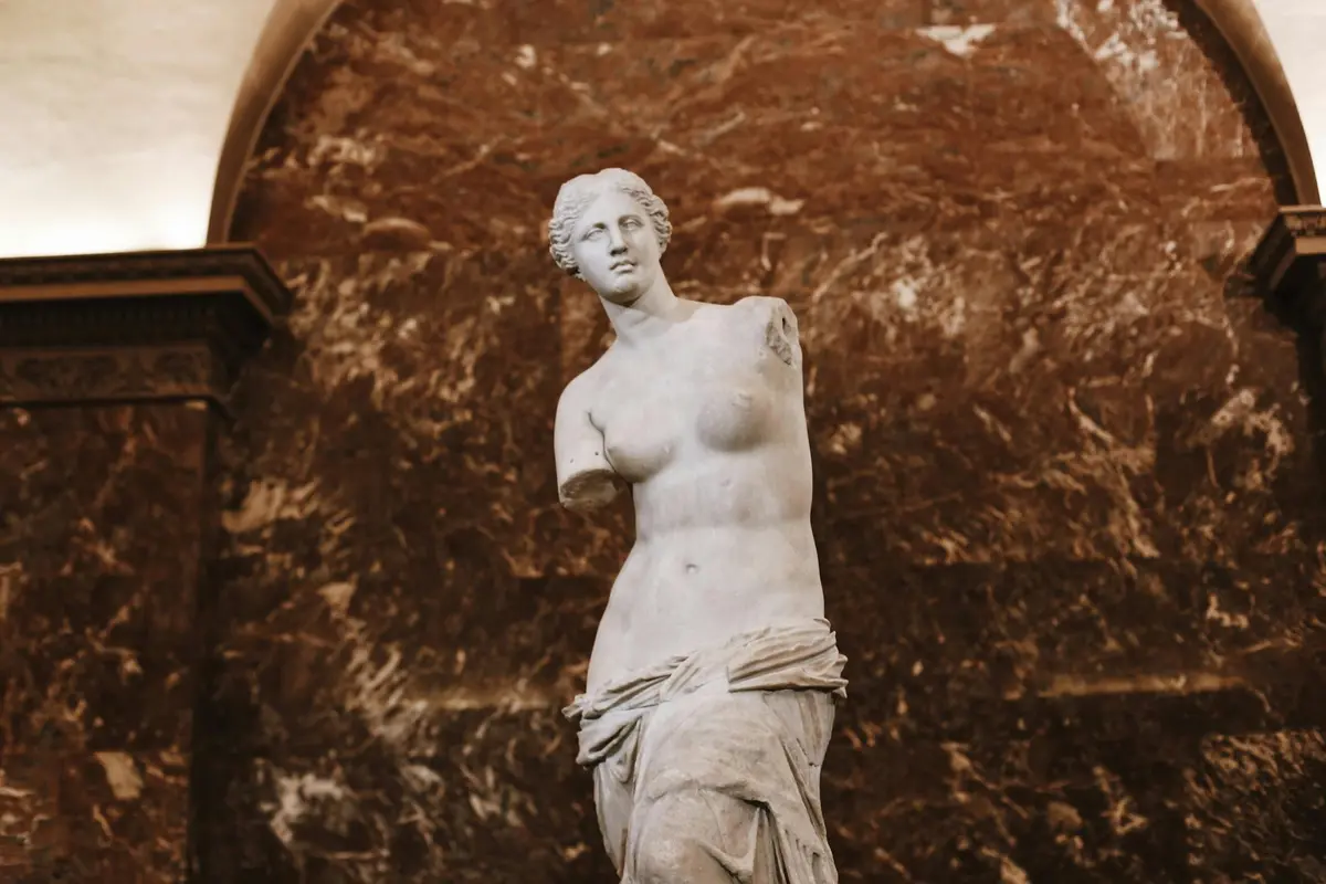 Statue en marbre d'une femme partiellement drapée et sans bras sur fond de marbre foncé.