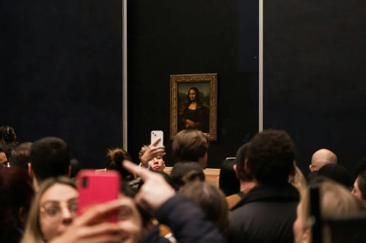 Une foule de personnes prenant des photos de la Joconde exposée sur un mur.