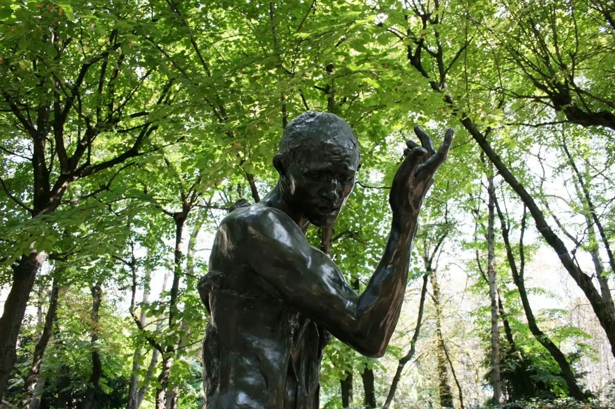 Une statue en bronze d'un homme au bras tendu sur fond d'arbres verdoyants.