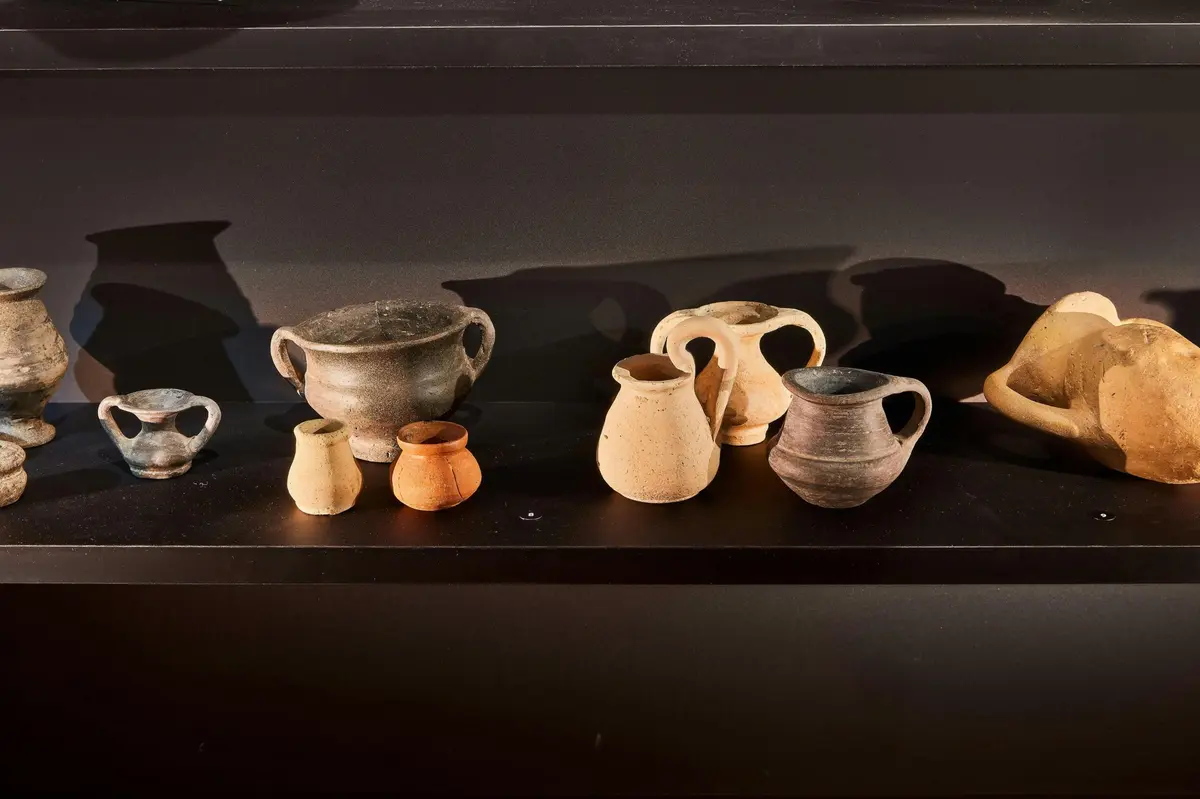 Un assortiment de petits pots et récipients en terre cuite exposés sur une étagère sombre.