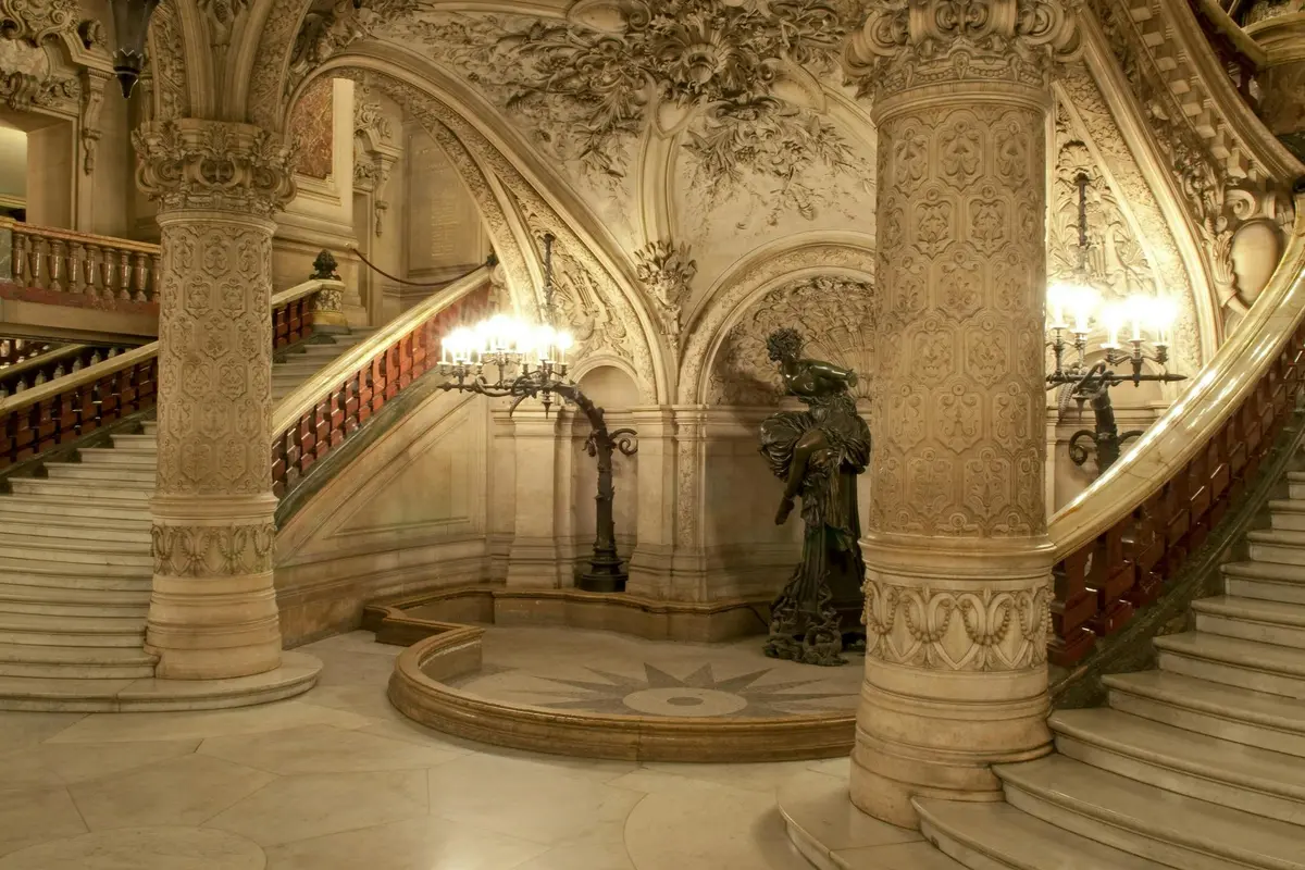 Escalier intérieur somptueux, orné de sculptures minutieuses, d'une grande statue et d'un éclairage décoratif, dans un cadre architectural grandiose.