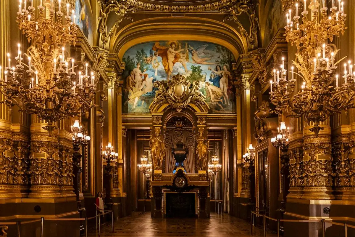 Une salle somptueuse avec un plafond peint, des ornements dorés, des lustres et une arche centrale ornée de sculptures raffinées.