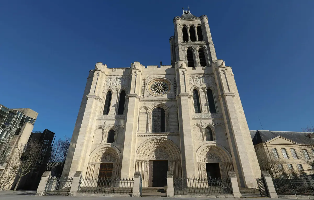 Une grande cathédrale de pierre ornée de fenêtres cintrées, de sculptures détaillées et d'un haut clocher sous un ciel bleu clair.