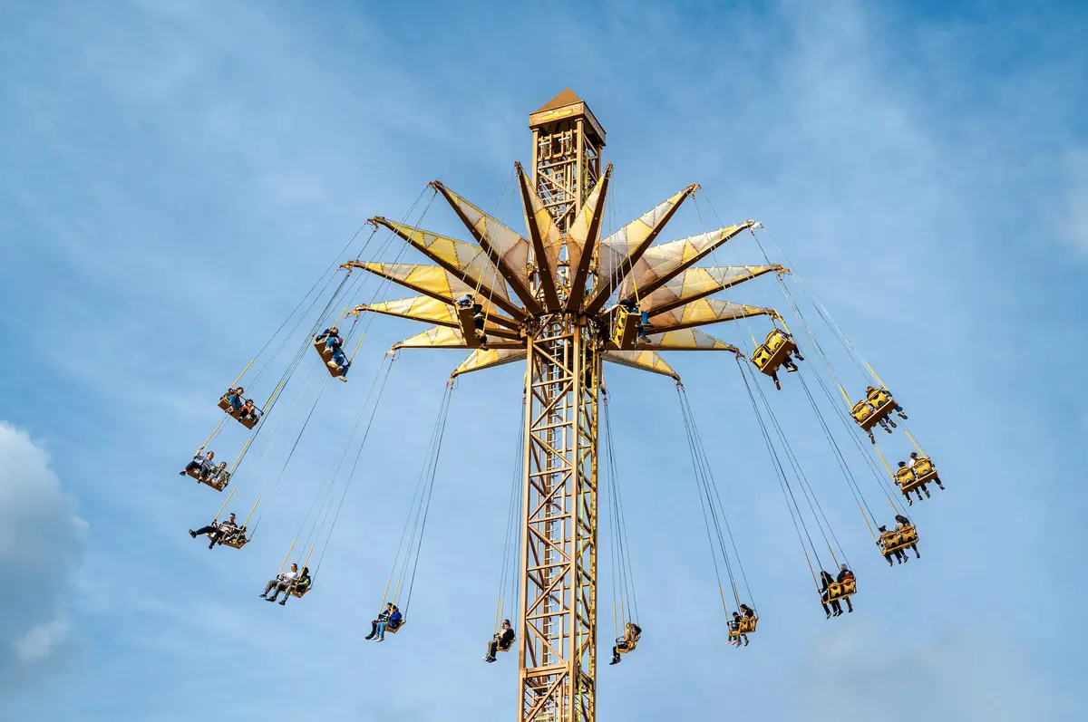 Un grand manège de parc d'attractions avec des personnes assises sur des balançoires, tournant très haut au-dessus du sol sous un ciel bleu.
