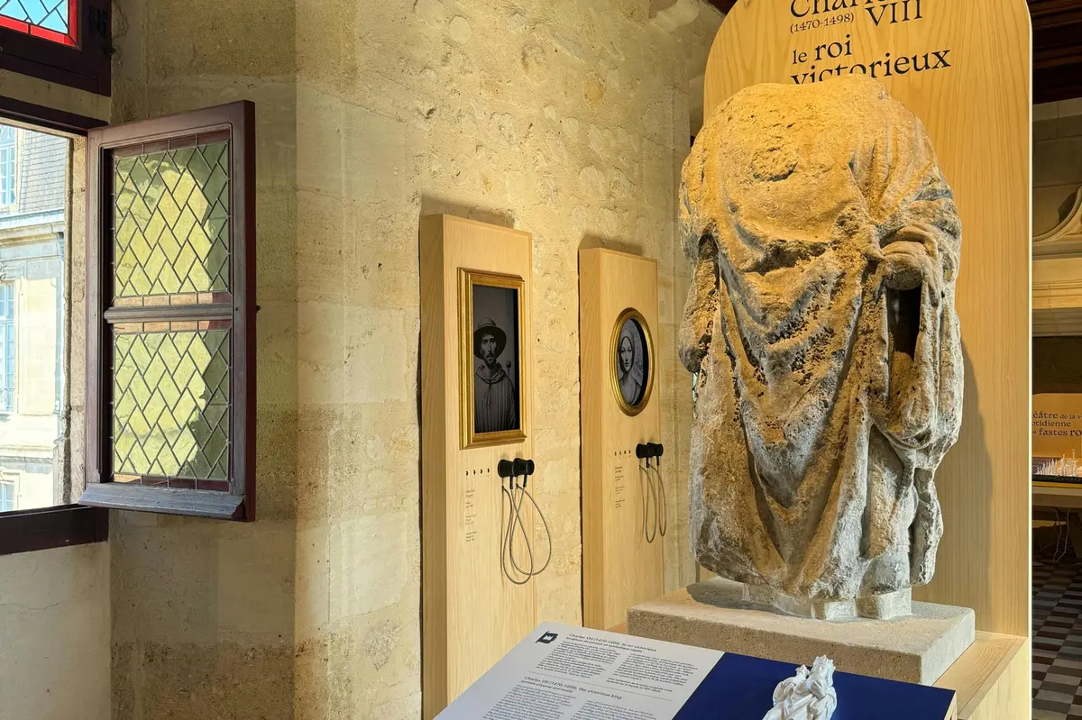 A stone statue and two portrait displays with headsets in a museum exhibit. A text panel and a window are also visible.