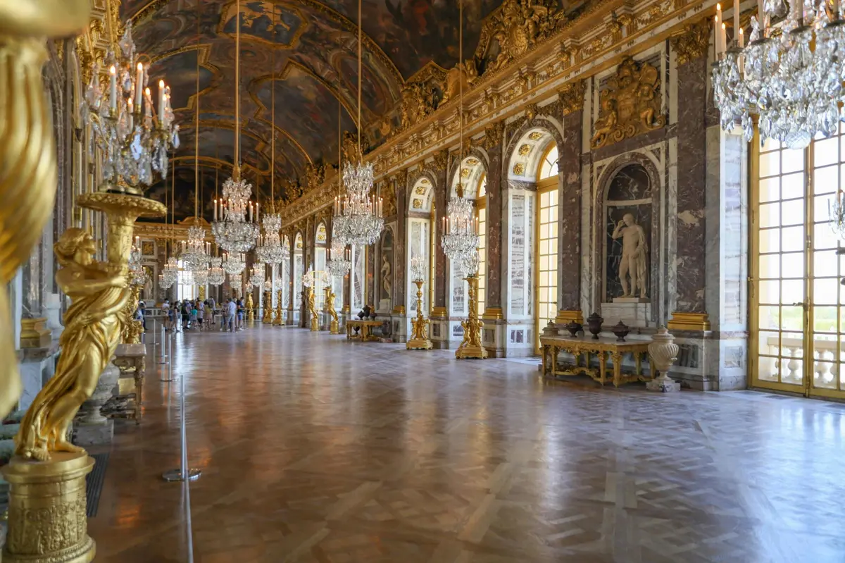 Une grande salle avec des lustres, des fenêtres cintrées, un décor orné et un sol poli, ressemblant à l'intérieur d'un palais historique.