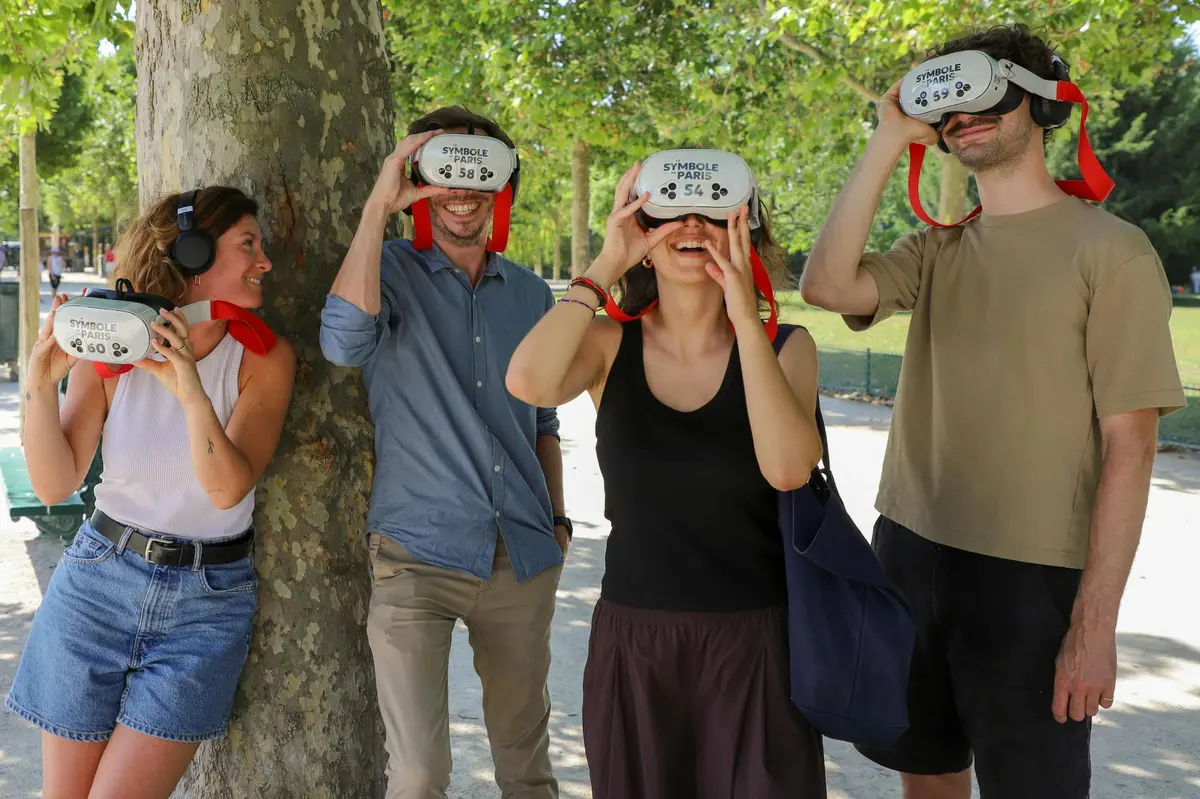 Quatre personnes à l'extérieur, équipées de casques de réalité virtuelle, debout près d'un arbre, avec un parc ensoleillé en arrière-plan.