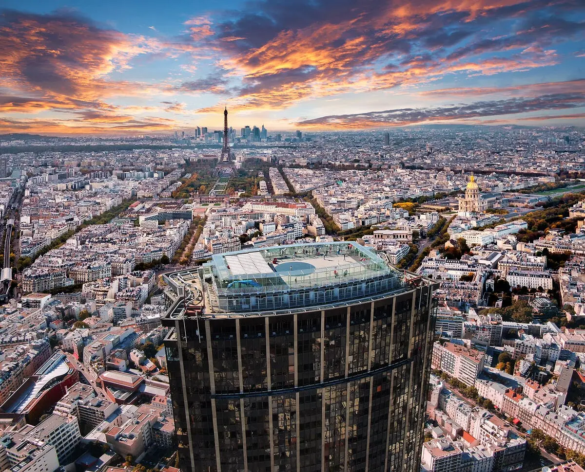 Vue aérienne de Paris avec un gratte-ciel au premier plan, la Tour Eiffel au loin et un ciel coloré au coucher du soleil.