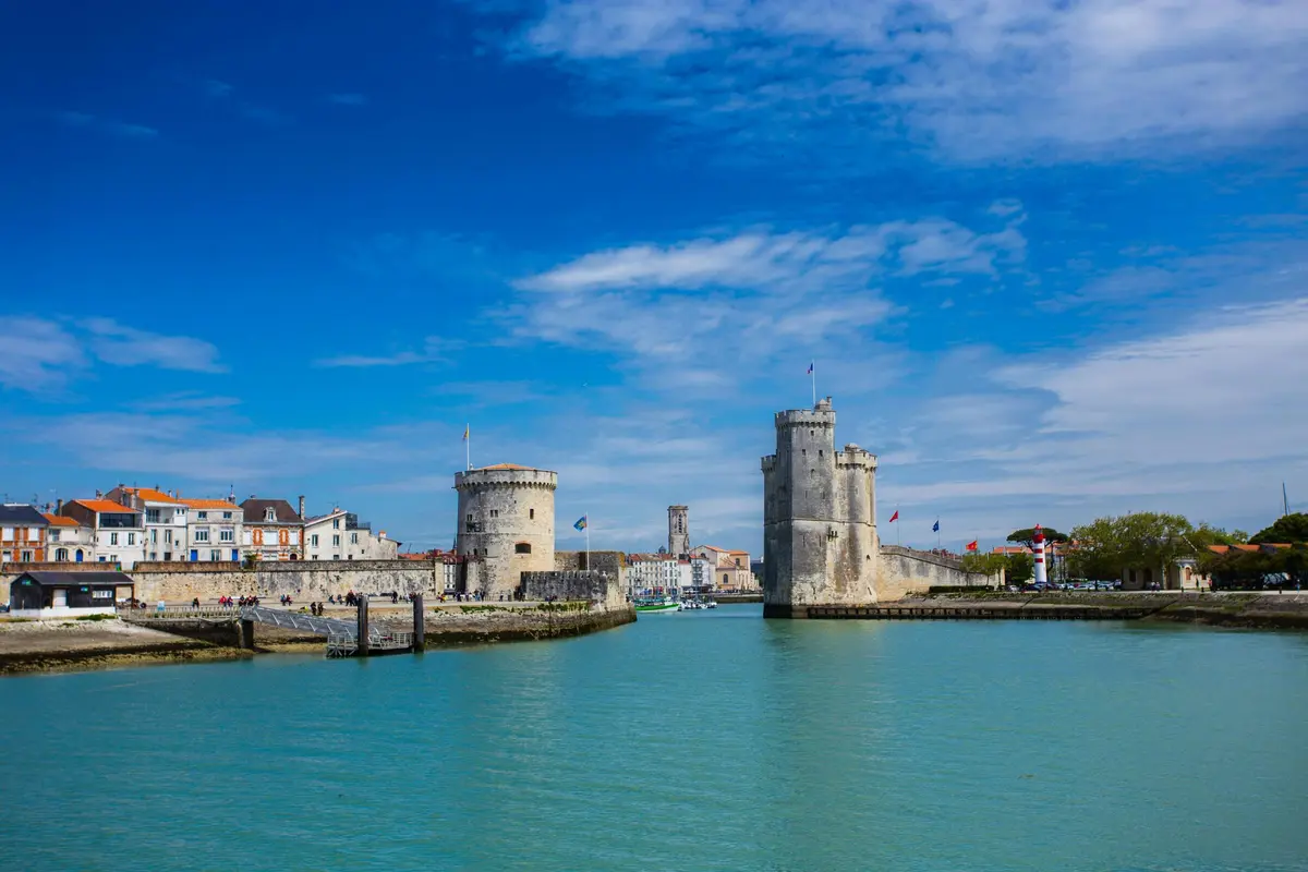 Tours historiques et bâtiments au bord de l'eau sous un ciel bleu éclatant, au bord d'une voie d'eau calme et turquoise.