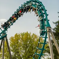 Des personnes montent sur des montagnes russes en boucle dont la piste est de couleur sarcelle, sur fond d'arbres verts et de ciel clair. &copy; Walibi Rhone Alpes