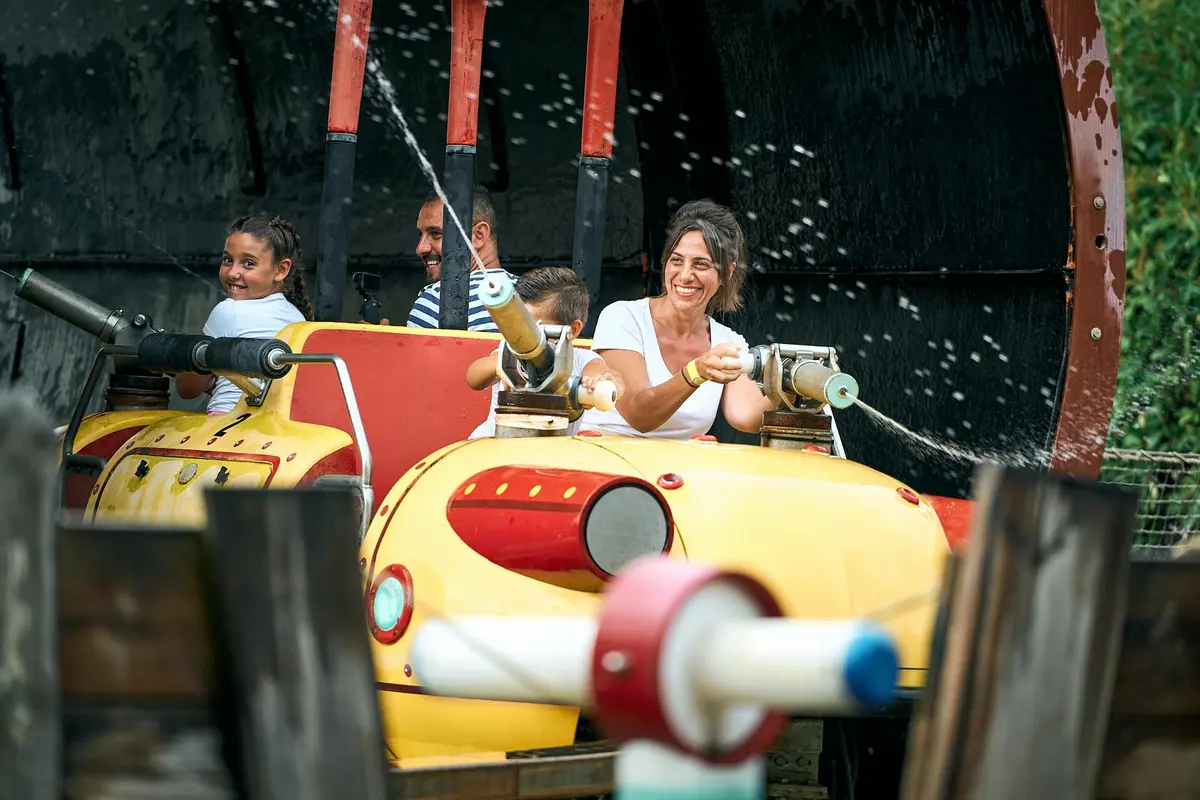 Des personnes s'amusent sur un manège aquatique, en utilisant des canons à eau pour projeter des jets d'eau. Tout le monde sourit et participe à l'activité.
