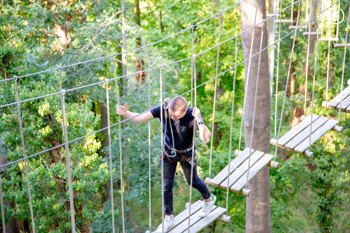 Une personne équipée d'un équipement de sécurité navigue sur un pont de corde situé au milieu des arbres d'une forêt.