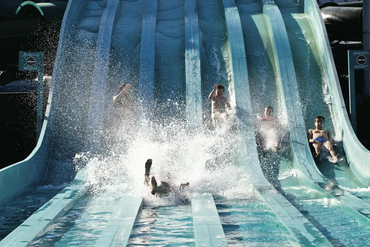 Quatre personnes glissent sur des toboggans parallèles, et deux d'entre elles se jettent dans la piscine au fond.
