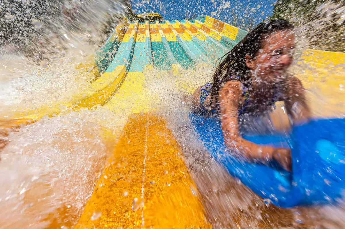 Une personne glisse sur un toboggan aquatique coloré sur un tapis bleu, avec de l'eau qui éclabousse autour d'elle.