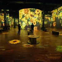 Une installation artistique immersive mettant en scène de grands tournesols numériques projetés sur les murs et le sol, devant un public de spectateurs. &copy; Culturespaces___Cyrille_de_la_Motte_Rouge