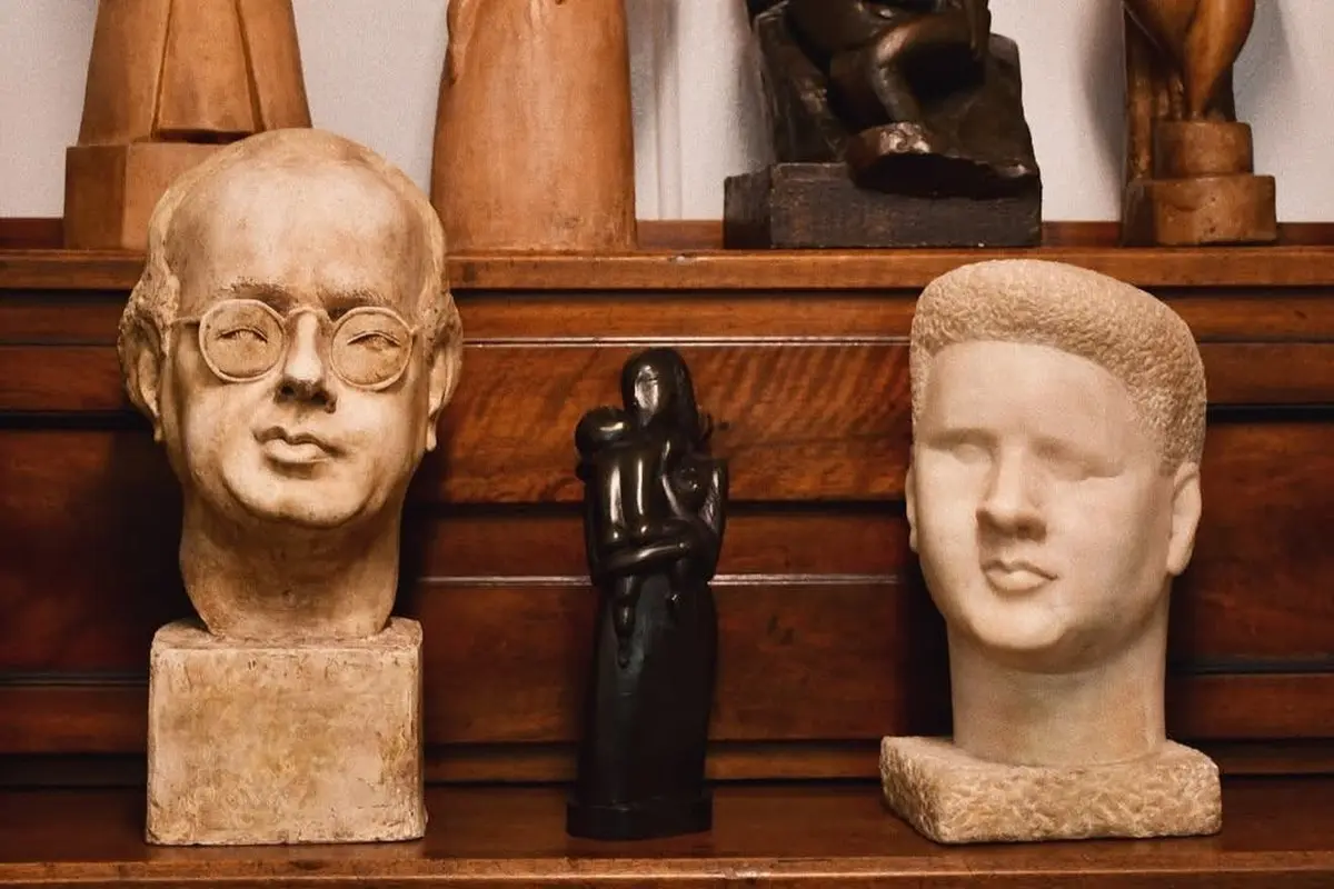 Une collection de sculptures sur une étagère en bois, comprenant deux bustes et une statue figurative abstraite centrale.